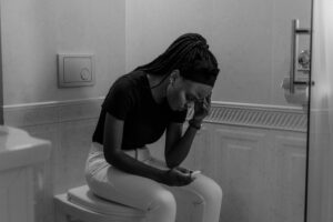 Black and white image of a young woman holding a pregnancy test, displaying anxiety.